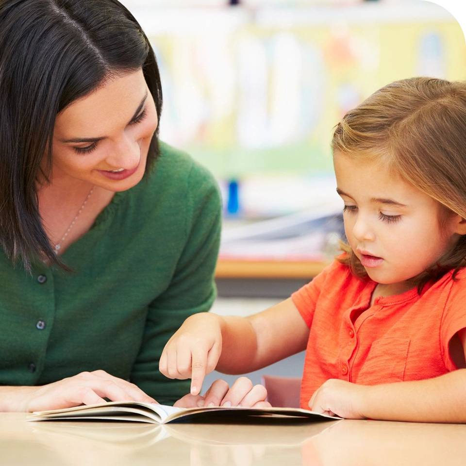 A therapist reading and pointing at a book with a young girl