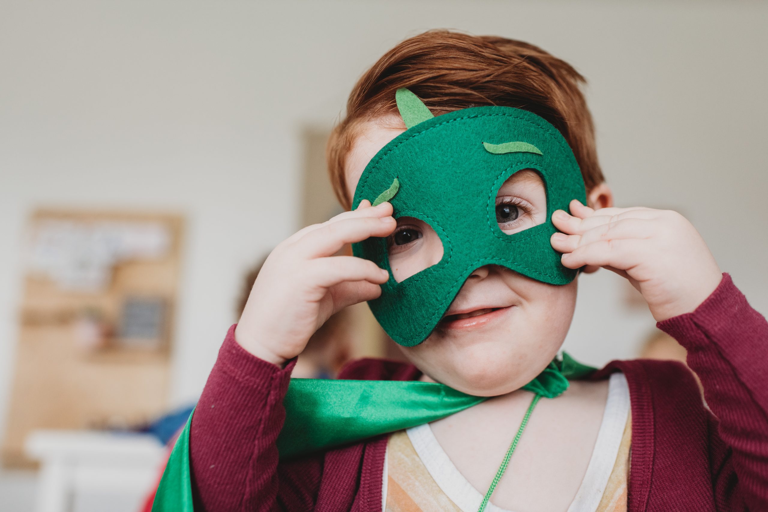 A child playing dress-up with a green felt superhero mask